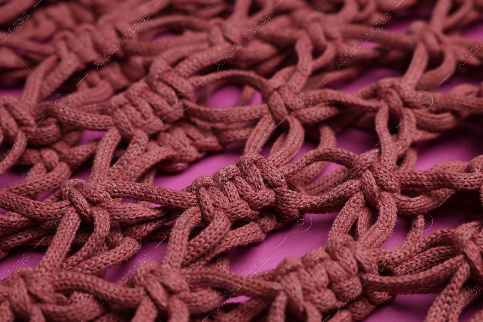 Photo of Handmade macrame shopping bag on crimson background, closeup