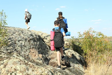 Photo of Family climbing on stones outdoors on sunny day, back view