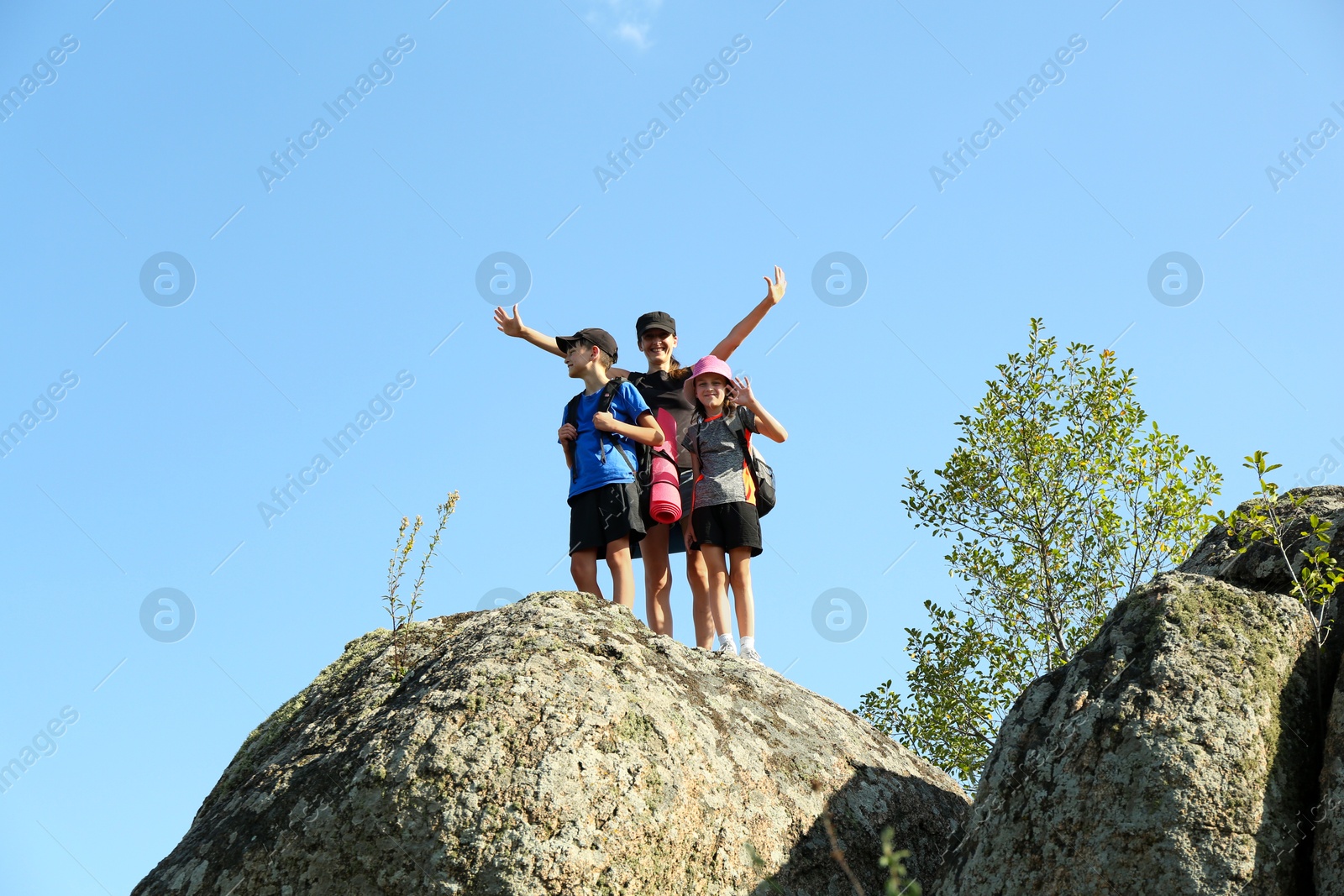 Photo of Cute family enjoying picturesque landscape on stone under blue sky, low angle view