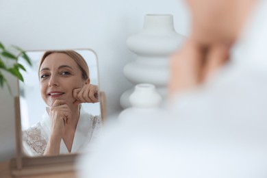 Photo of Smiling woman doing facial self massage near mirror at home