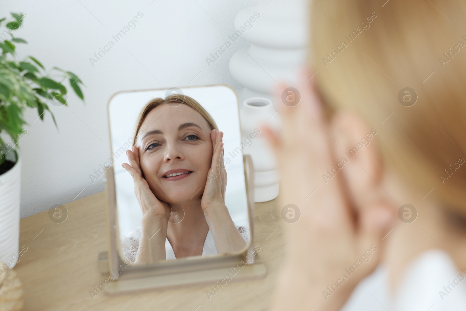 Photo of Smiling woman doing facial self massage near mirror at home