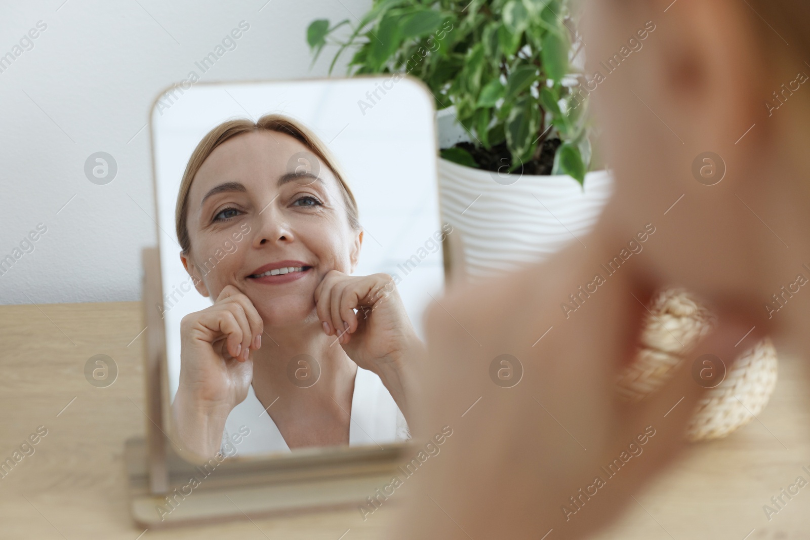 Photo of Smiling woman doing facial self massage near mirror at home