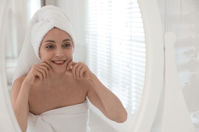 Photo of Smiling woman doing facial self massage near mirror in bathroom