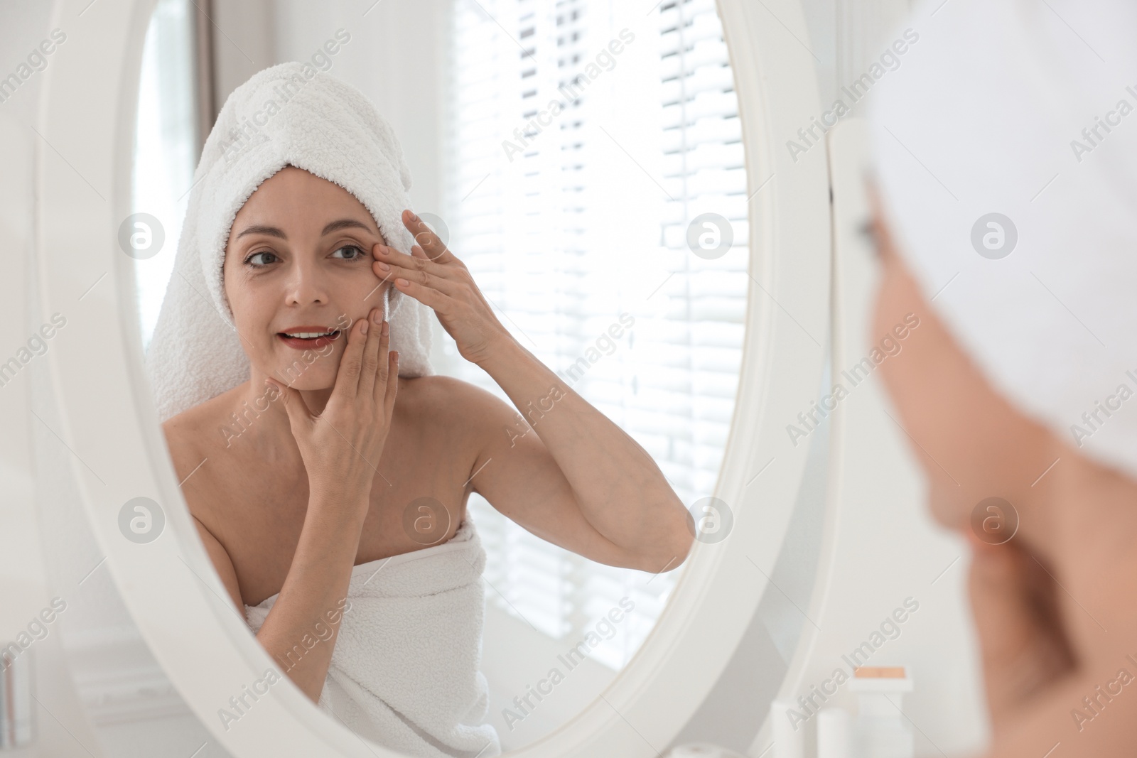 Photo of Beautiful woman doing facial self massage near mirror in bathroom