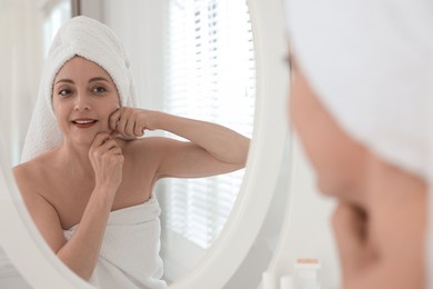 Photo of Smiling woman doing facial self massage near mirror in bathroom