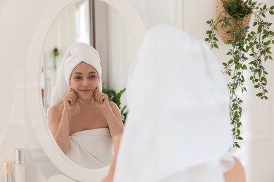 Photo of Beautiful woman doing facial self massage near mirror in bathroom