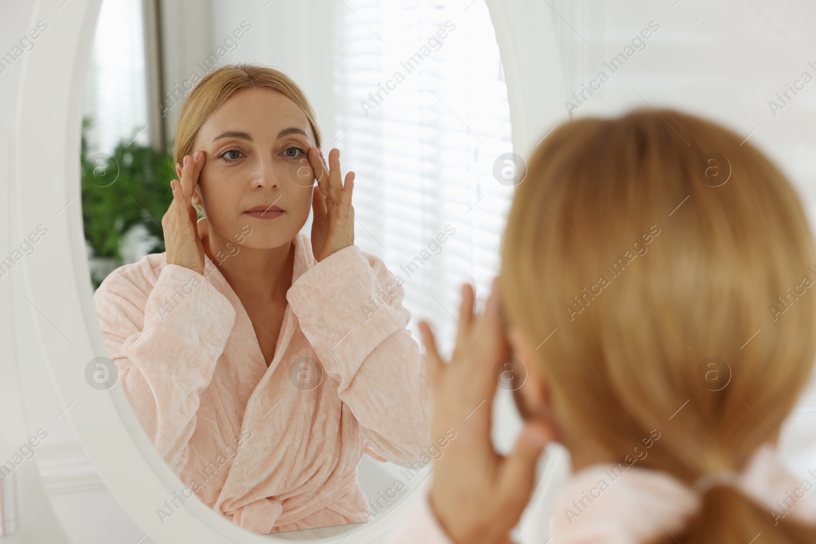 Photo of Beautiful woman doing facial self massage near mirror in bathroom