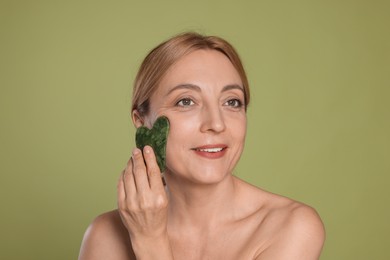 Photo of Smiling woman doing facial self massage with gua sha tool on green background