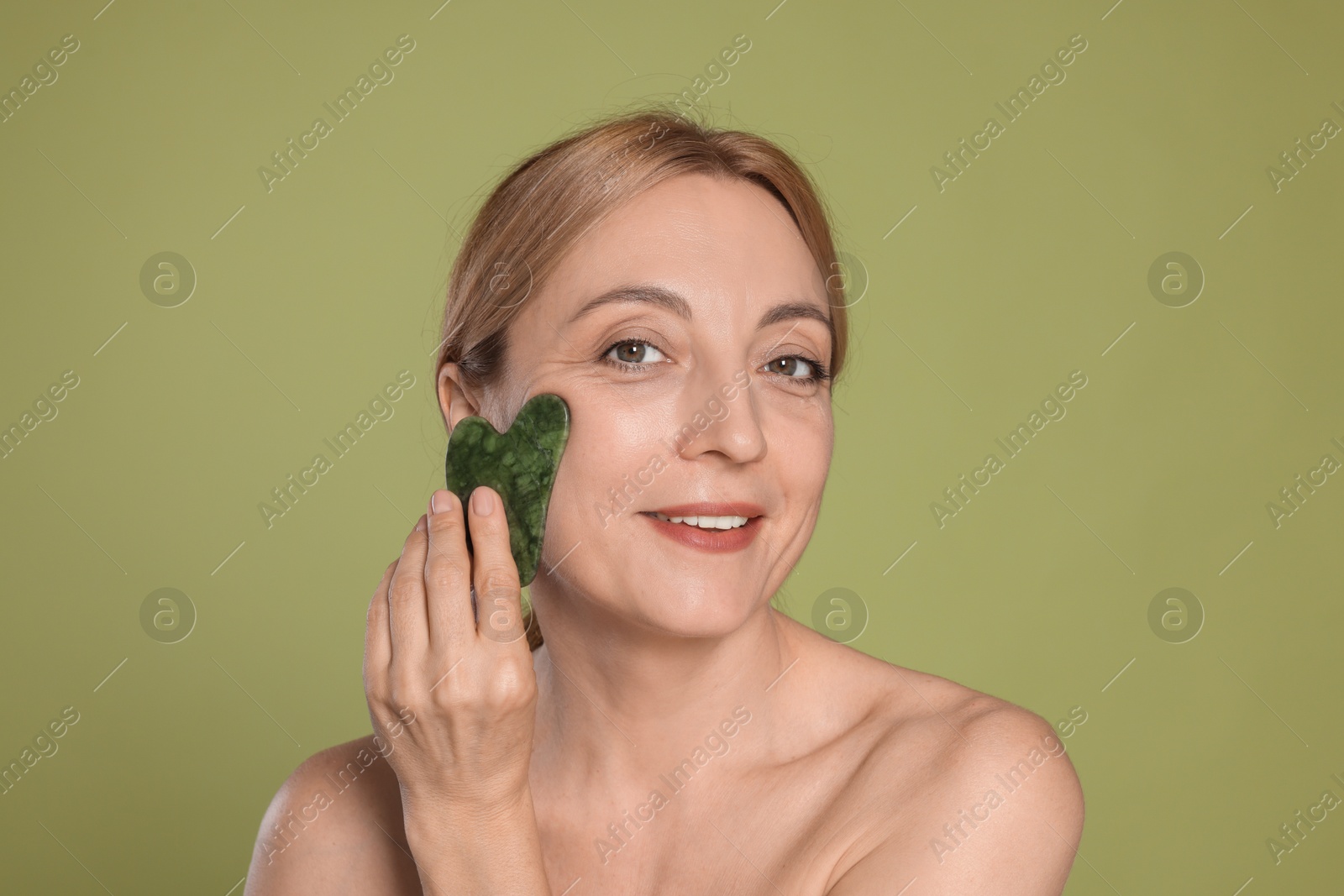 Photo of Smiling woman doing facial self massage with gua sha tool on green background