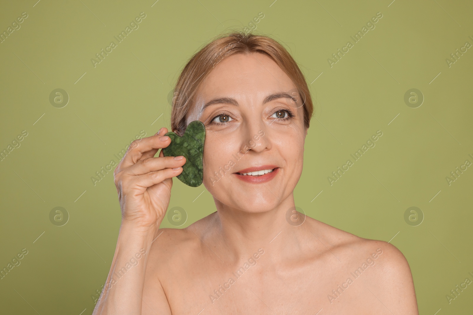 Photo of Beautiful woman doing facial self massage with gua sha tool on green background