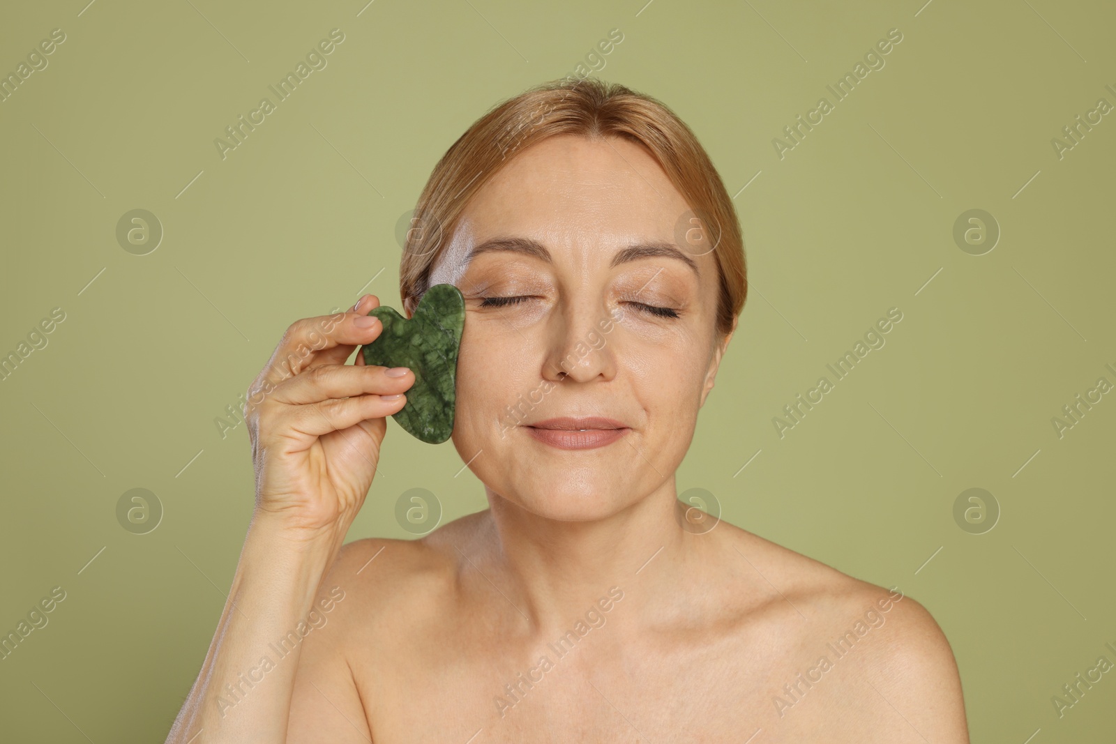 Photo of Beautiful woman doing facial self massage with gua sha tool on green background