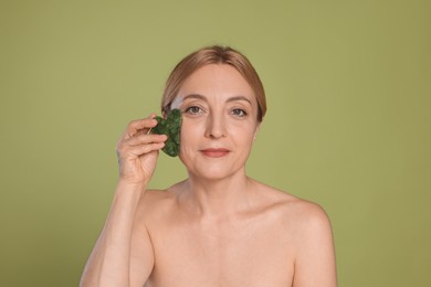 Photo of Beautiful woman doing facial self massage with gua sha tool on green background