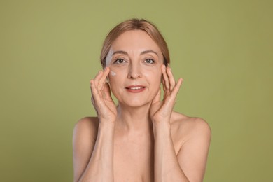 Smiling woman with cream on face doing self massage against green background