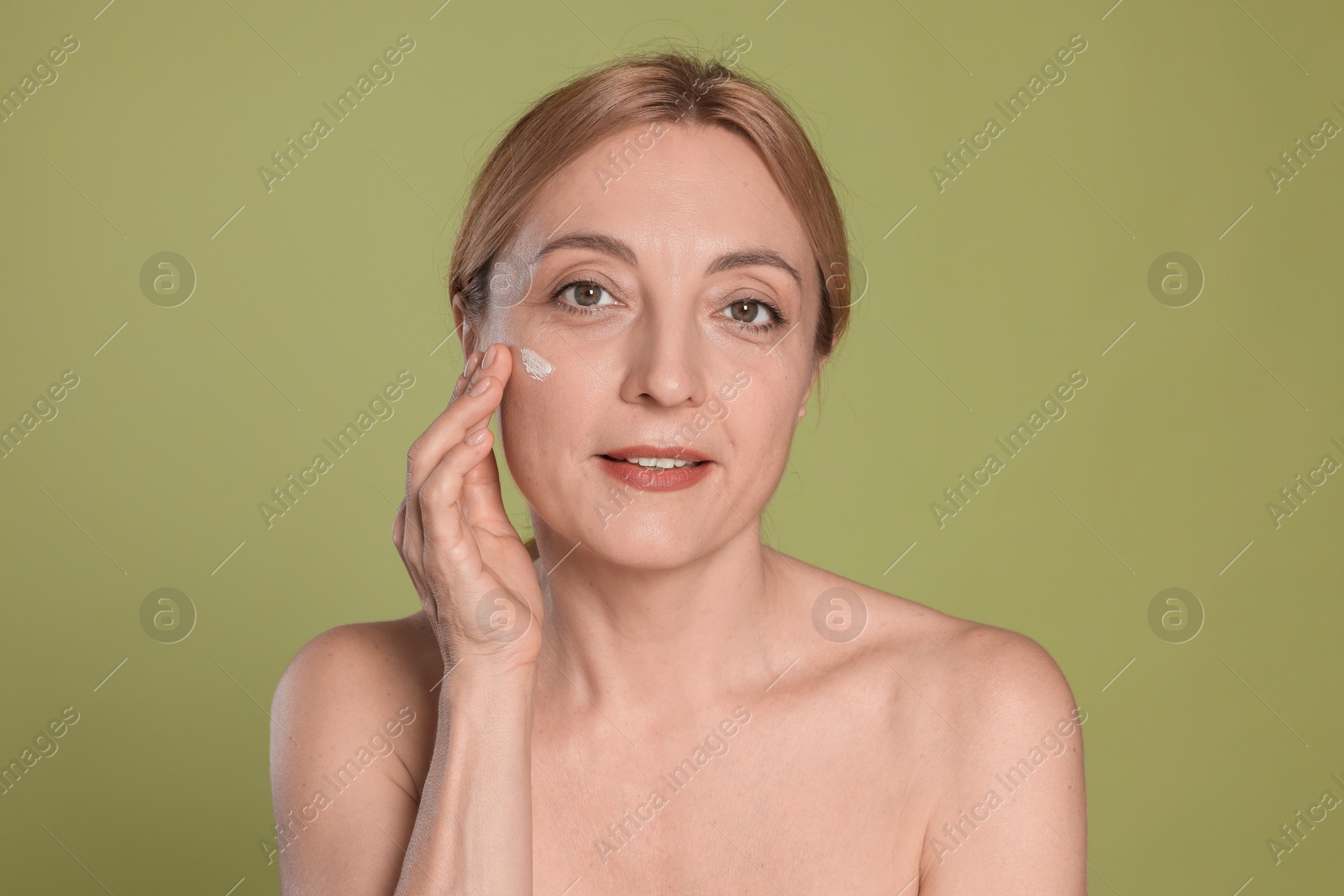 Photo of Beautiful woman with cream on face doing self massage against green background