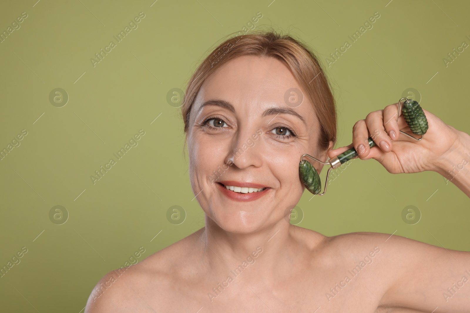 Photo of Smiling woman doing facial self massage with roller on green background