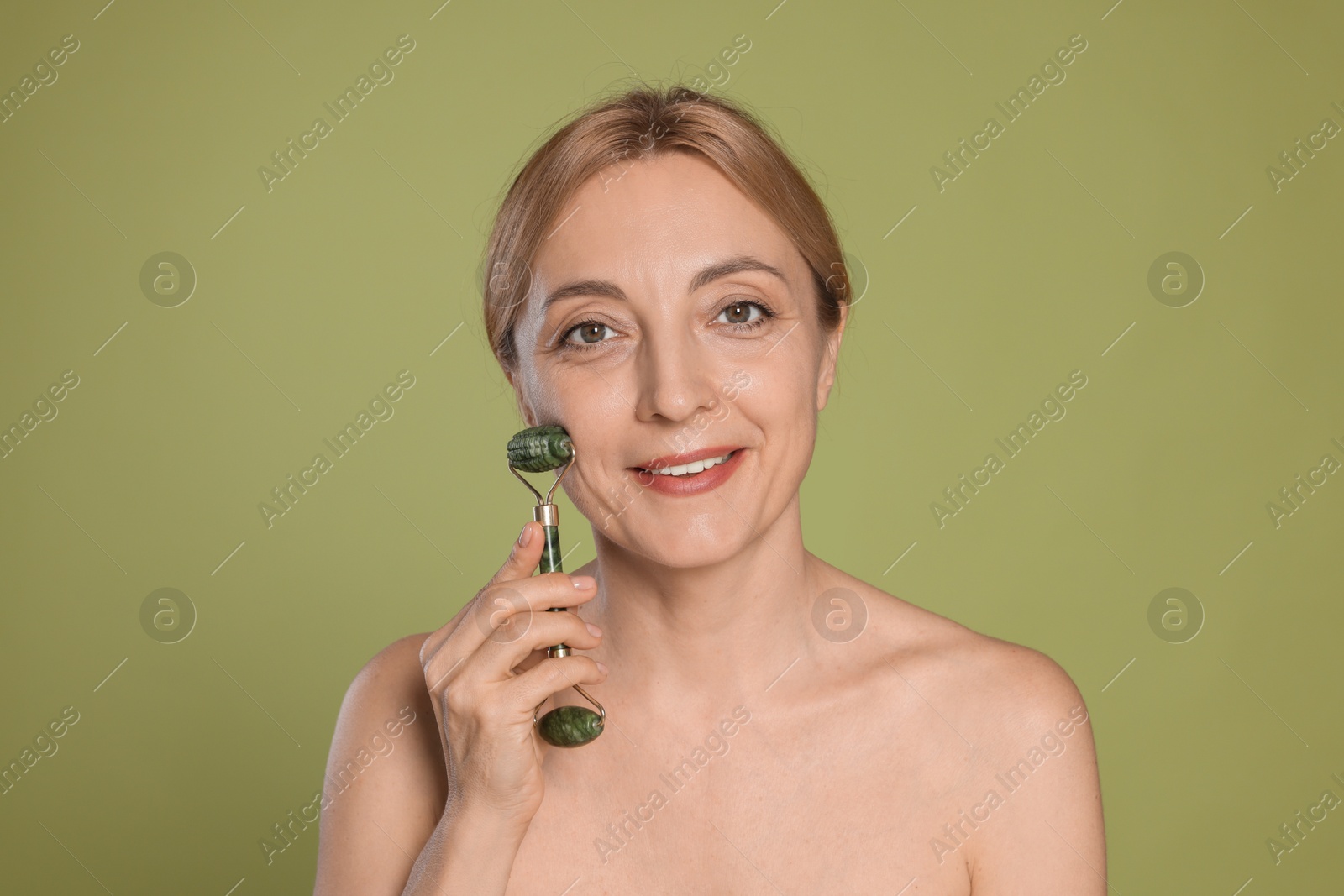 Photo of Smiling woman doing facial self massage with roller on green background