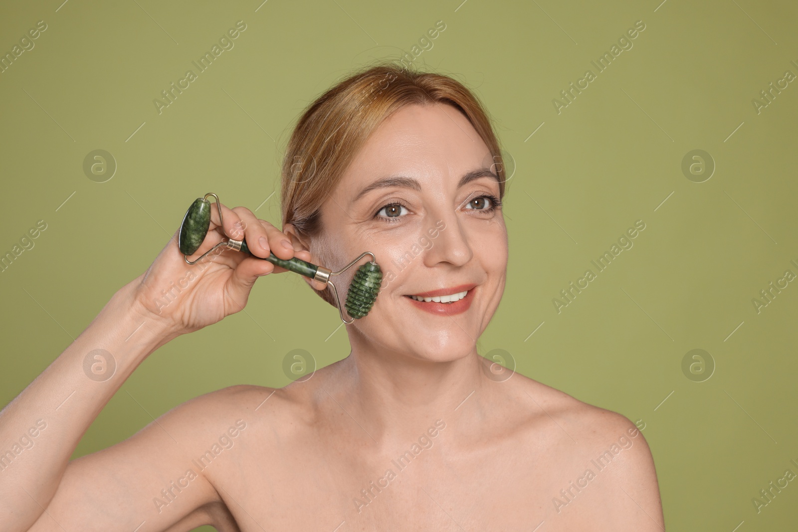 Photo of Smiling woman doing facial self massage with roller on green background