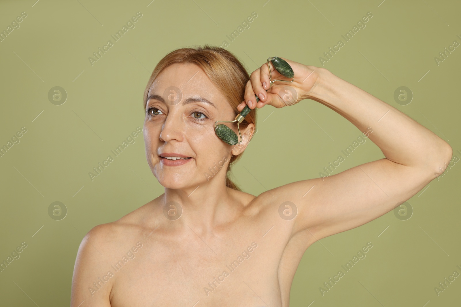 Photo of Beautiful woman doing facial self massage with roller on green background