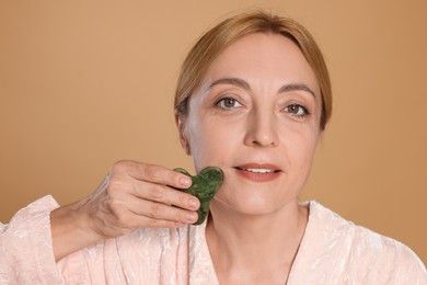 Photo of Smiling woman doing facial self massage with gua sha tool on beige background