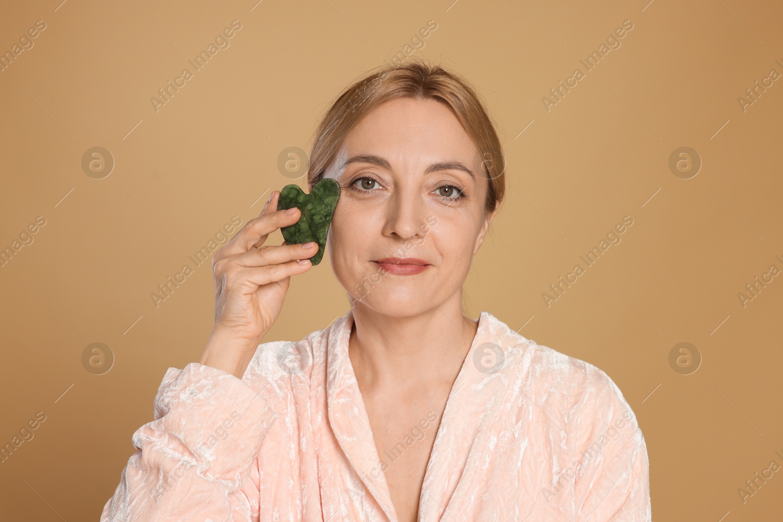 Photo of Beautiful woman doing facial self massage with gua sha tool on beige background