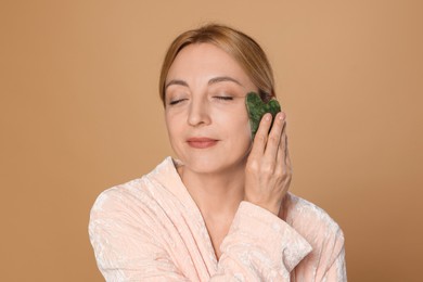 Photo of Beautiful woman doing facial self massage with gua sha tool on beige background