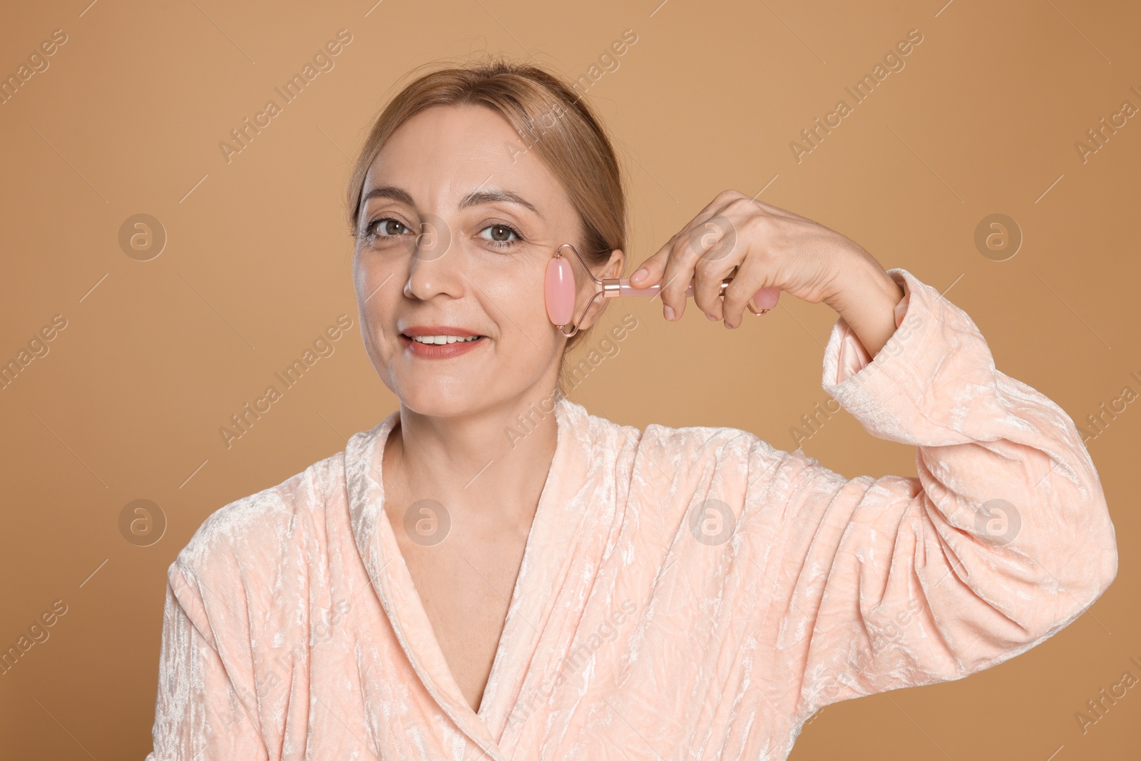 Photo of Smiling woman doing facial self massage with roller on beige background