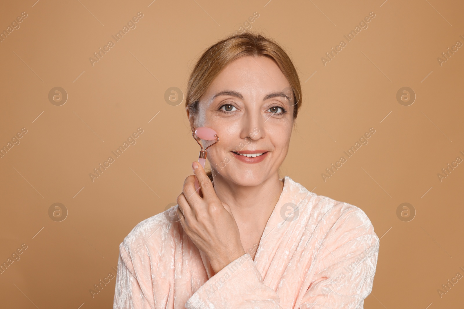 Photo of Smiling woman doing facial self massage with roller on beige background