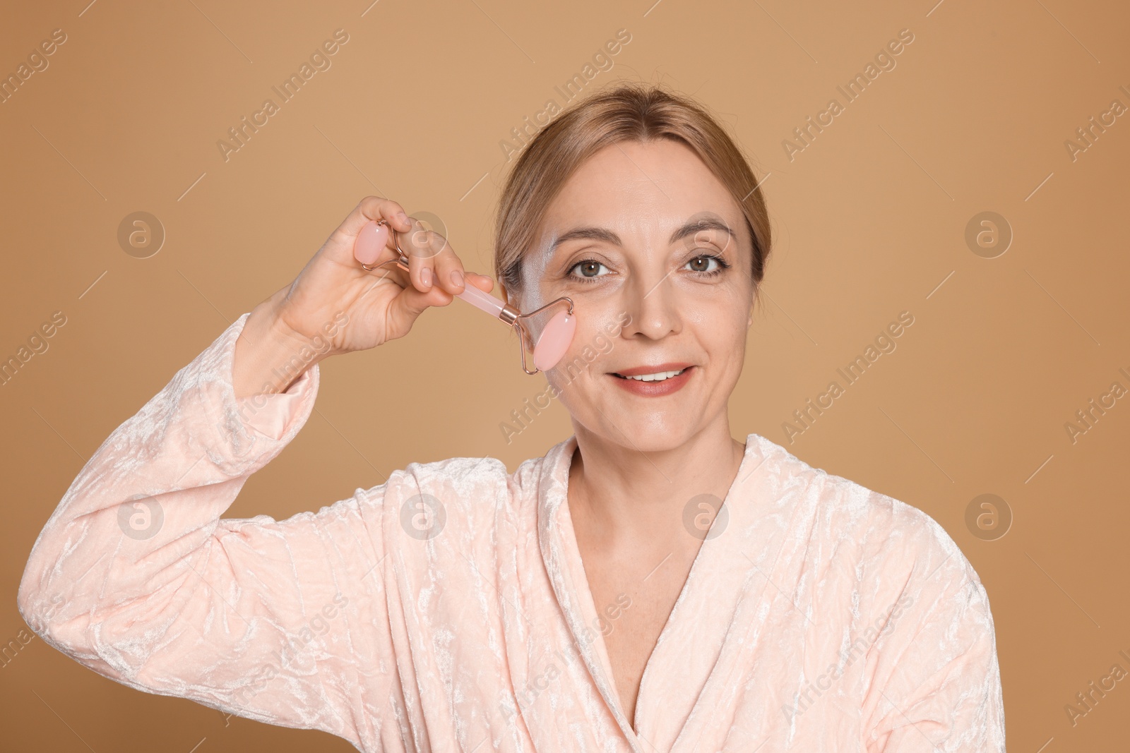 Photo of Smiling woman doing facial self massage with roller on beige background