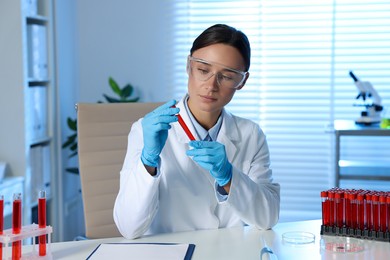 Laboratory testing. Doctor holding test tube with blood sample at table indoors