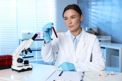 Photo of Laboratory testing. Doctor holding test tube with blood sample at table indoors