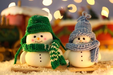 Photo of Cute decorative snowmen on artificial snow against blurred background, closeup