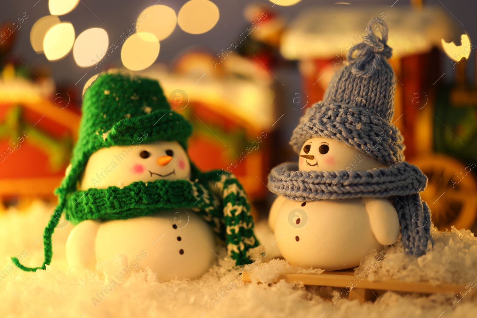 Photo of Cute decorative snowmen on artificial snow against blurred lights