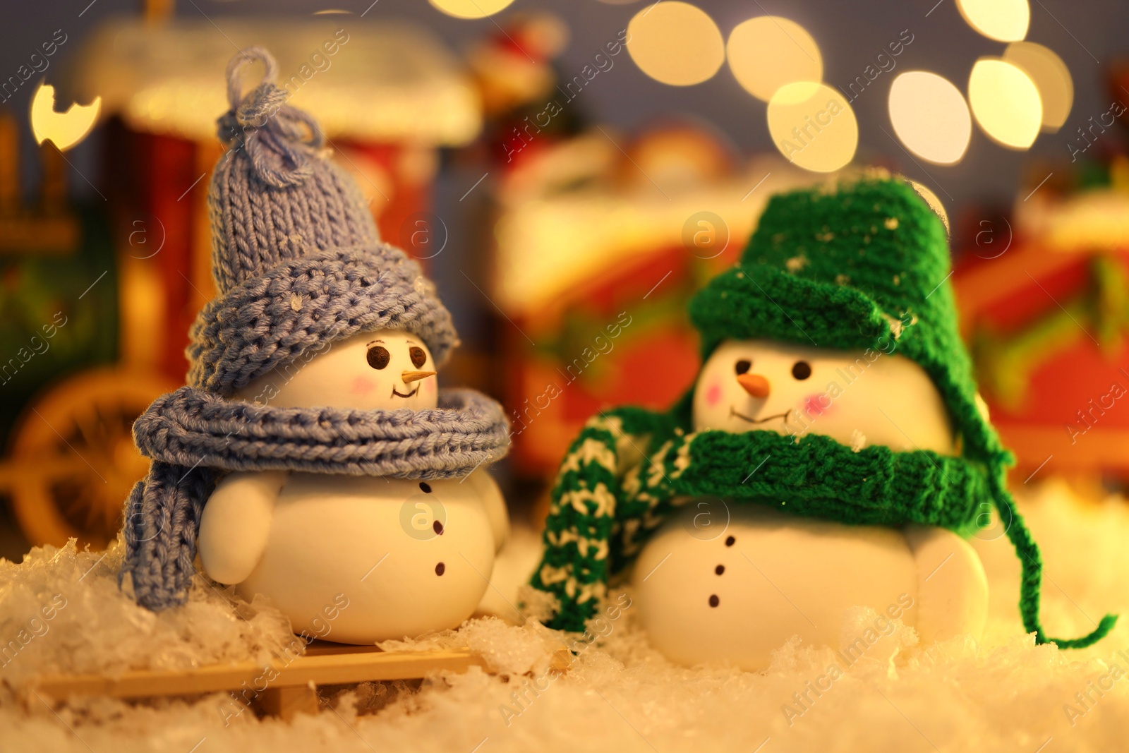 Photo of Cute decorative snowmen on artificial snow against blurred lights