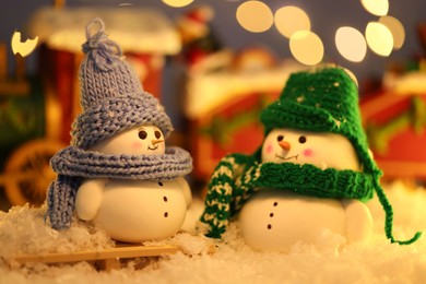 Photo of Cute decorative snowmen on artificial snow against blurred lights