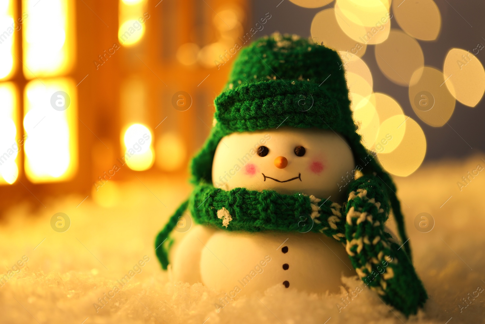 Photo of Cute decorative snowman on artificial snow against blurred lights, closeup