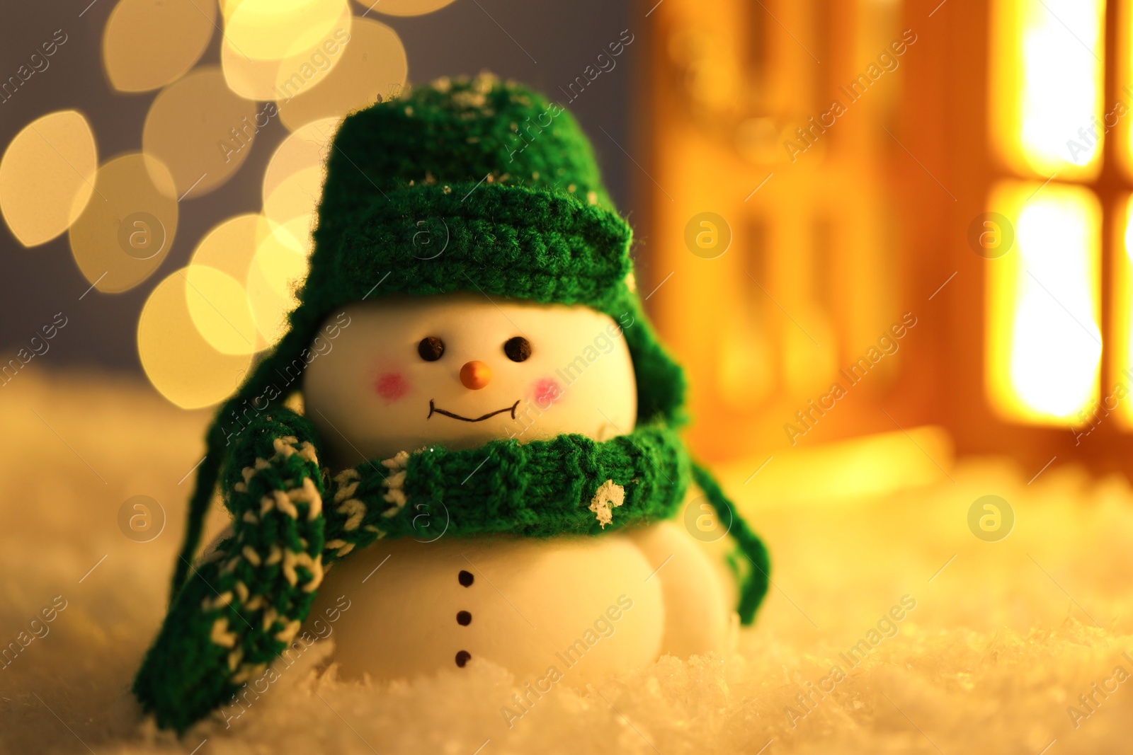 Photo of Cute decorative snowman on artificial snow against blurred lights, closeup