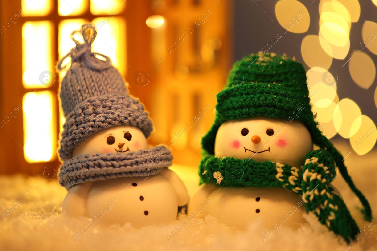 Photo of Cute decorative snowmen on artificial snow against blurred lights, closeup