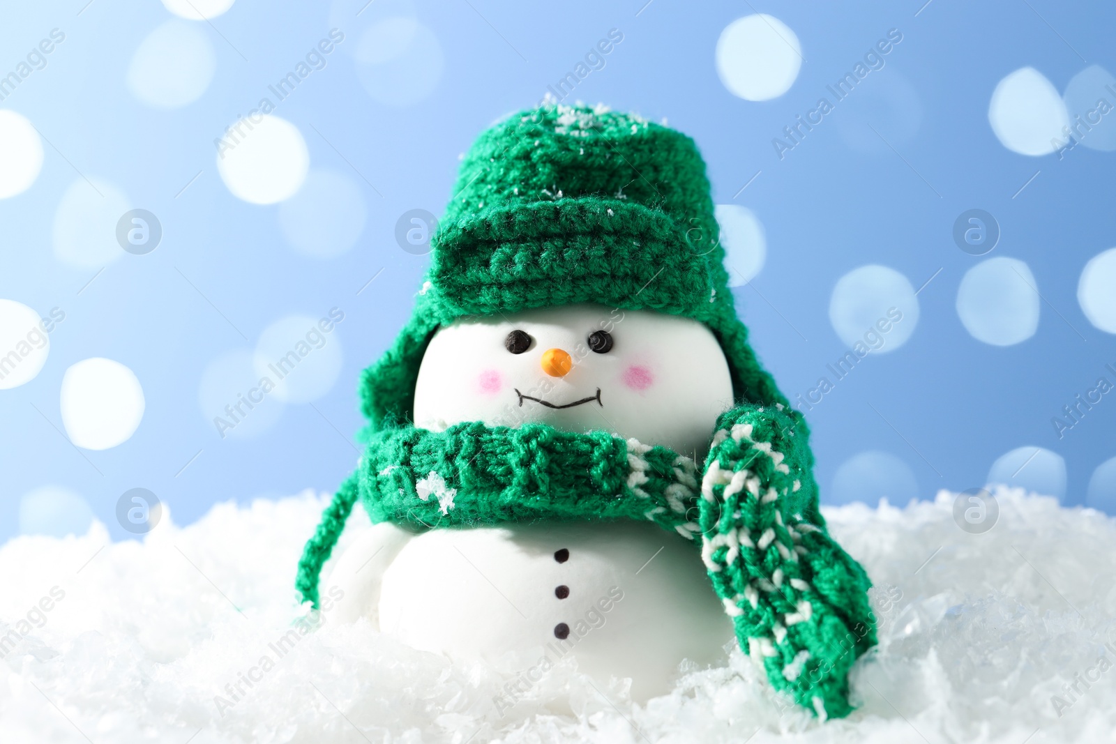 Photo of Cute decorative snowman on artificial snow against light blue background, closeup