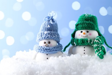 Photo of Cute decorative snowmen on artificial snow against light blue background