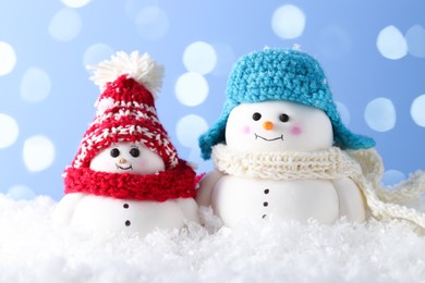 Photo of Cute decorative snowman on artificial snow against light blue background with blurred lights, closeup