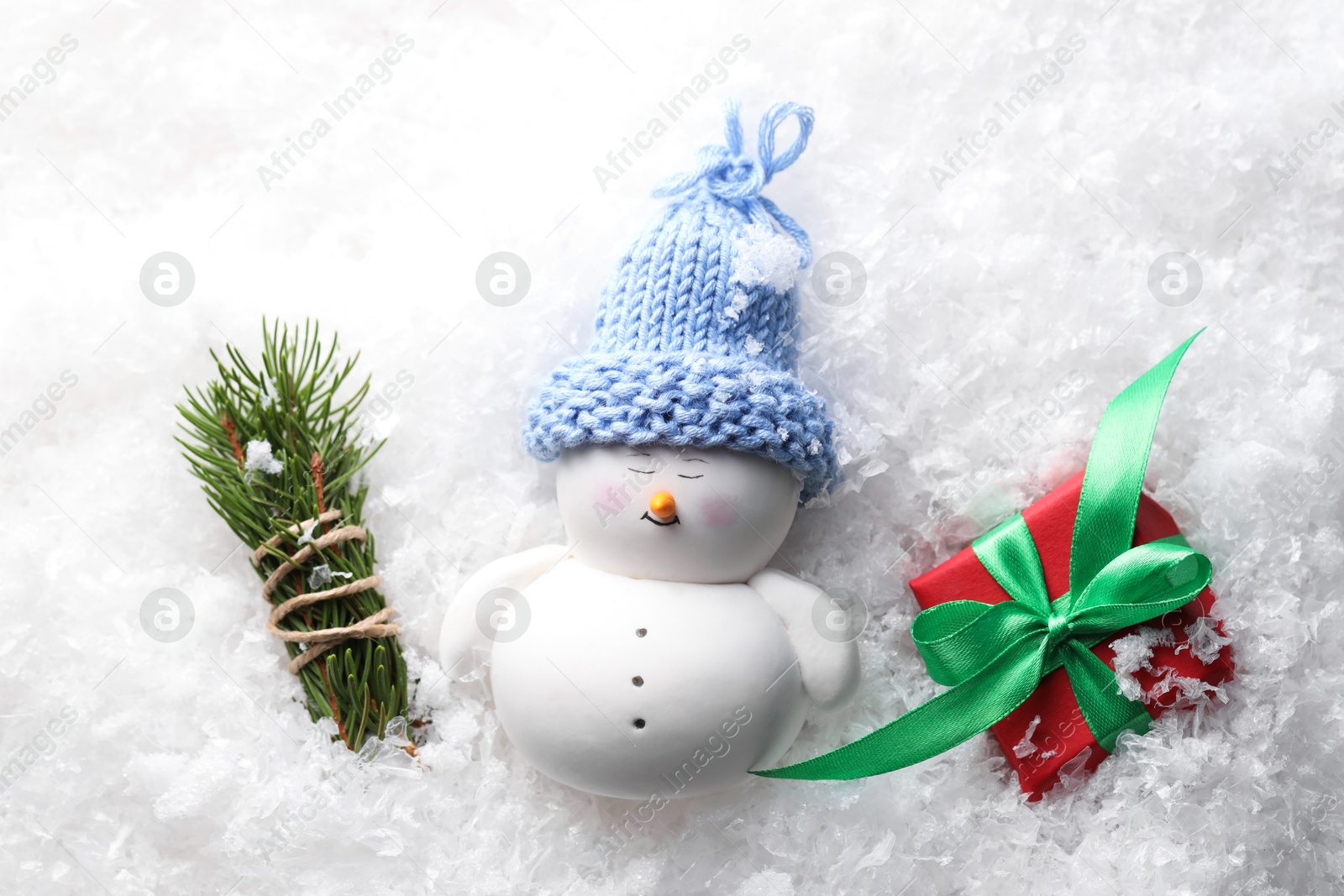 Photo of Cute decorative snowman, fir tree branches and gift box on artificial snow, flat lay