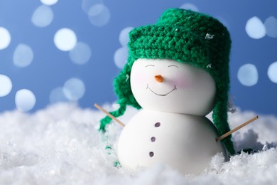 Photo of Cute decorative snowman on artificial snow against light blue background with blurred lights, closeup. Space for text