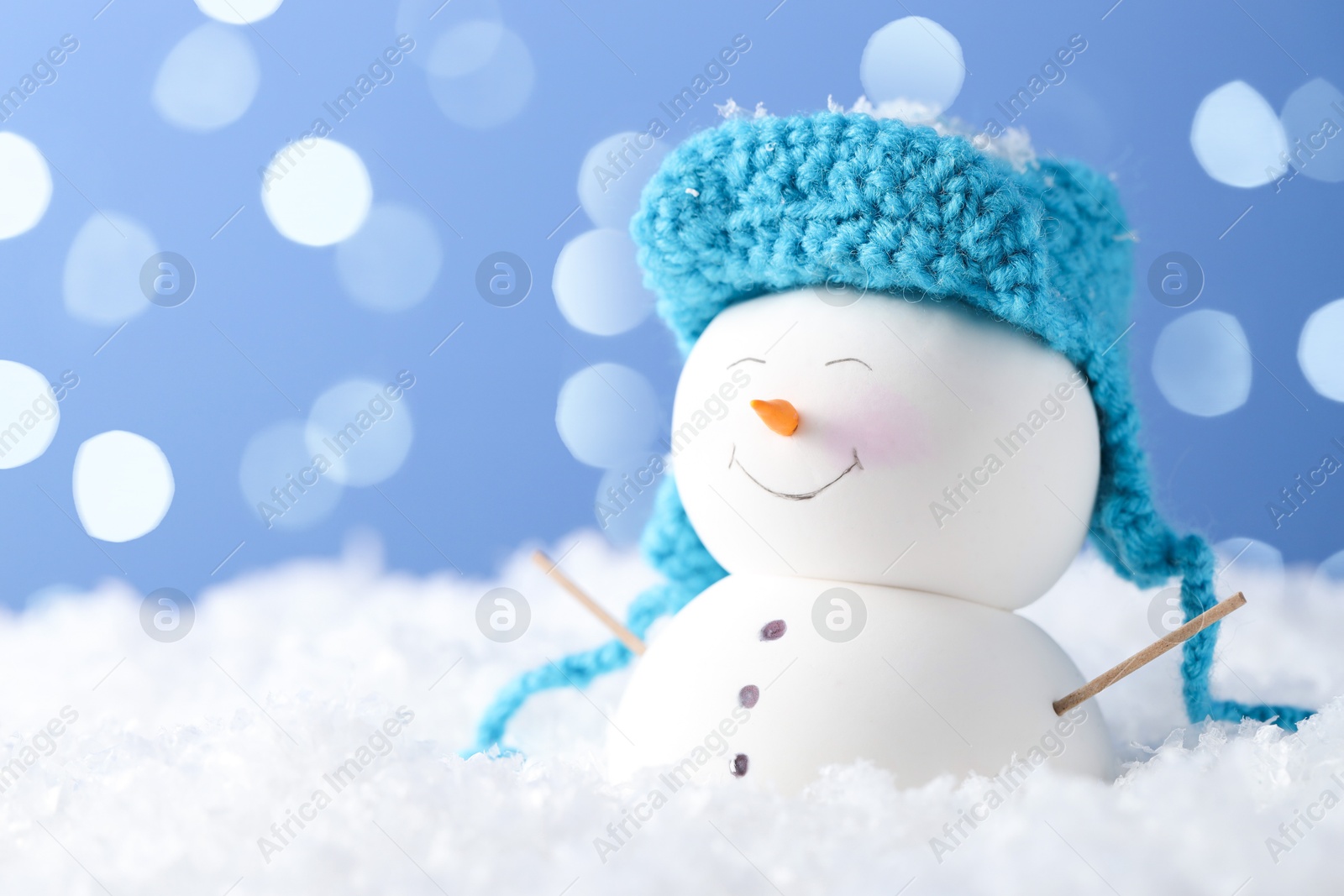 Photo of Cute decorative snowman on artificial snow against light blue background with blurred lights, closeup. Space for text