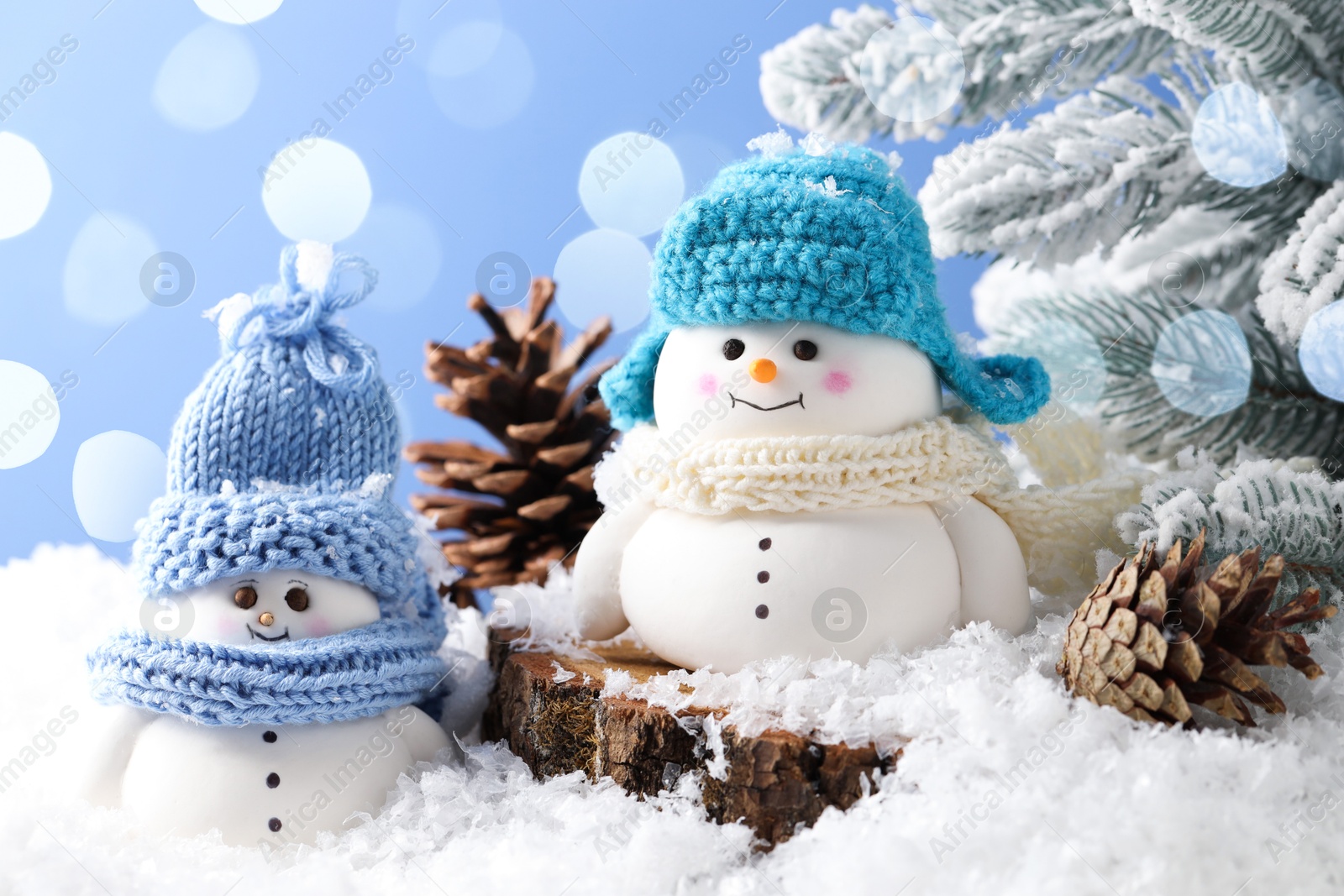 Photo of Cute decorative snowmen, fir tree branches and cones on artificial snow against light blue background, closeup