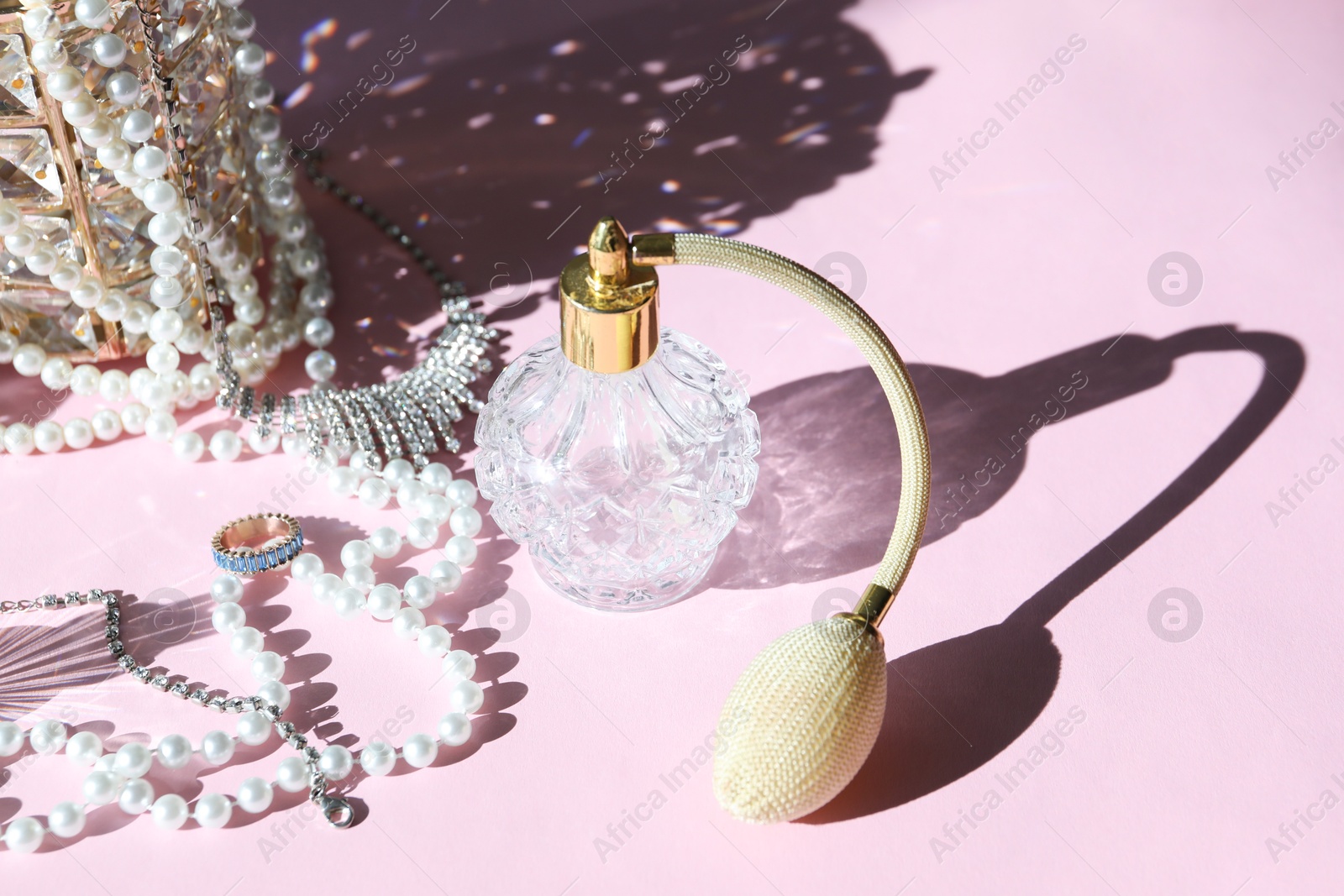 Photo of Bottle of perfume and stylish jewelry on pink background with shadows