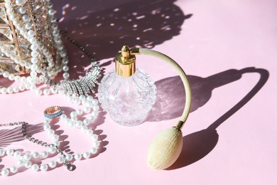 Photo of Bottle of perfume and stylish jewelry on pink background with shadows