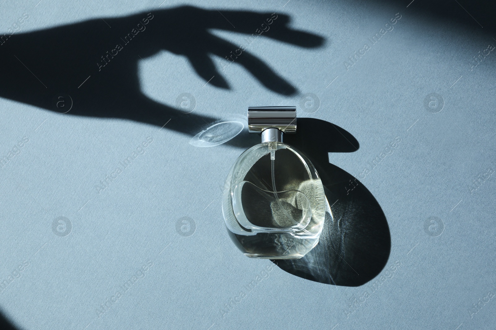 Photo of Perfume bottle and shadow of woman's hand on grey background, top view