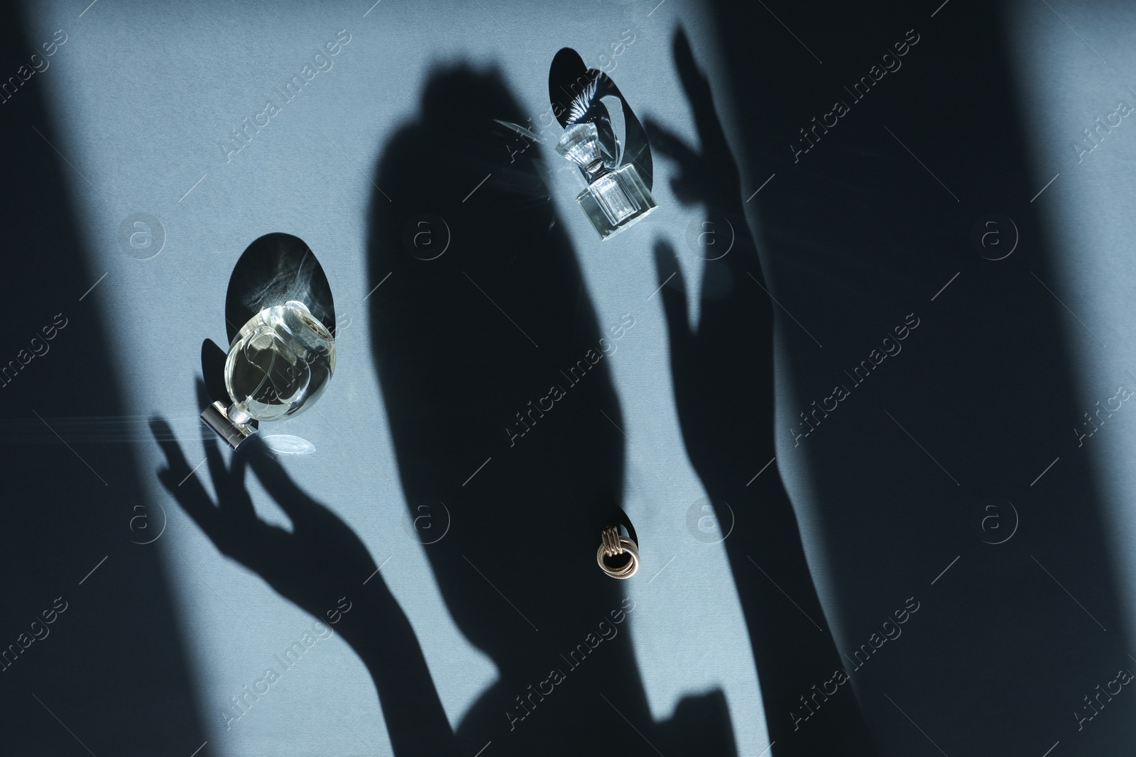 Photo of Perfume bottles, earring and woman's shadow on grey background, top view