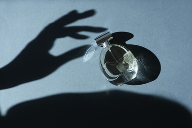 Photo of Perfume bottle and shadow of woman's hand on grey background, top view