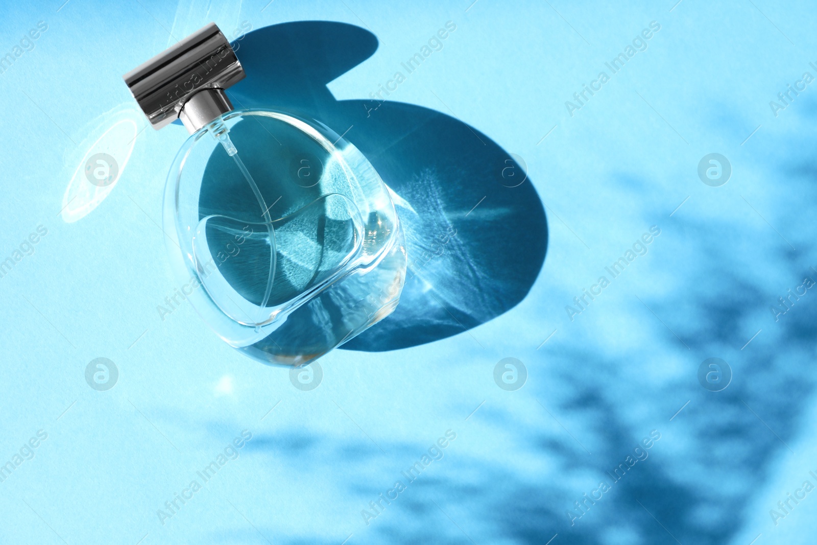 Photo of Perfume bottle casting shadow on light blue background, top view